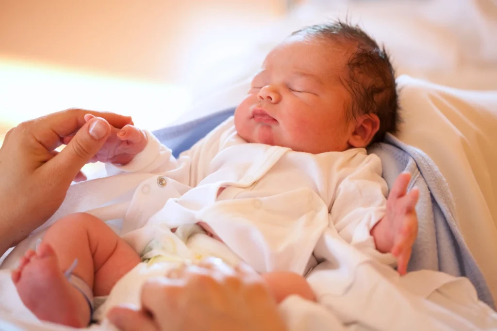 Newborn baby resting while a parent gently holds their hand